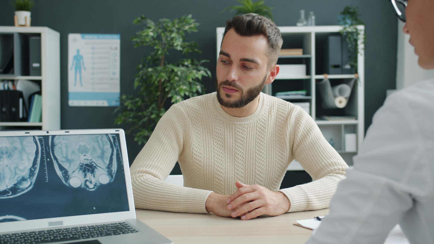 Arzt bespricht Gehirnscan-Ergebnisse mit Patientin am Laptop.